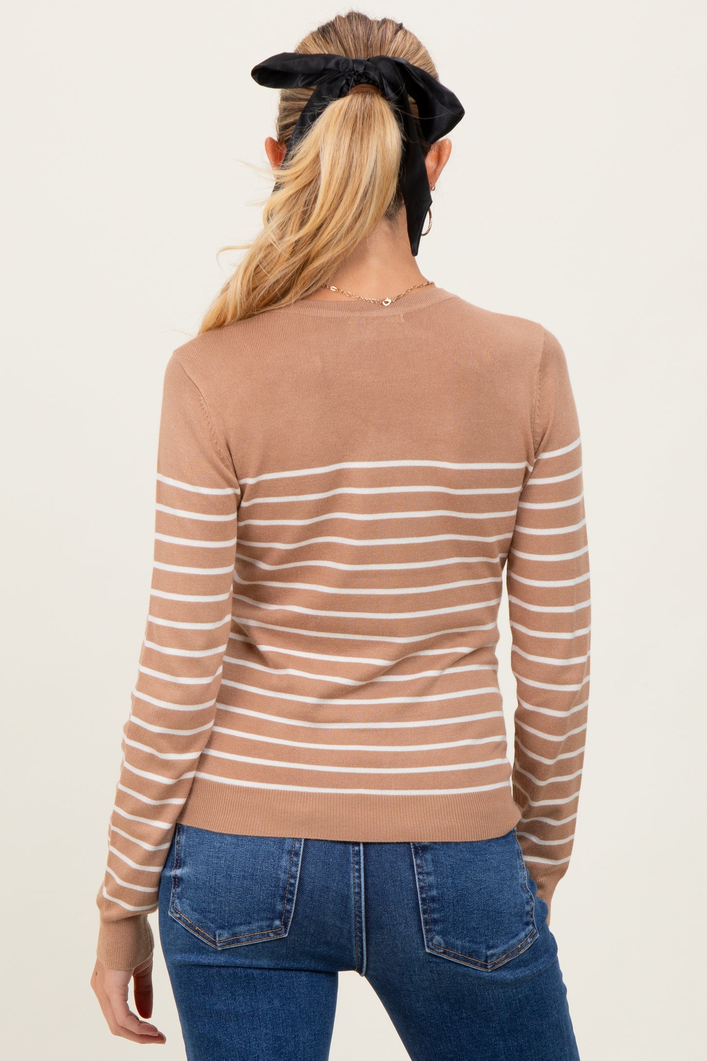 woman wearing a tan striped maternity sweater and blue jeans, viewed from the back with hair tied in a black bow