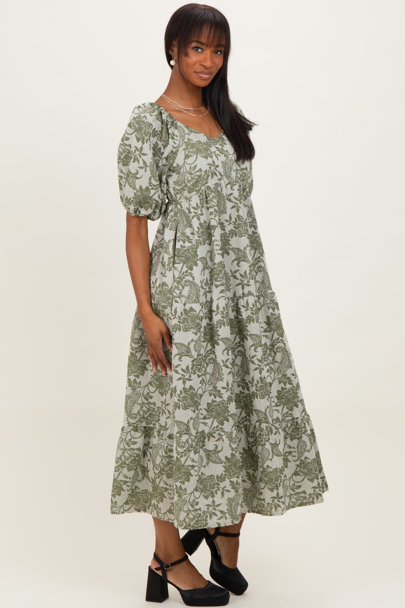 woman wearing a green floral print midi dress with puff sleeves and a tiered skirt, standing against a plain background