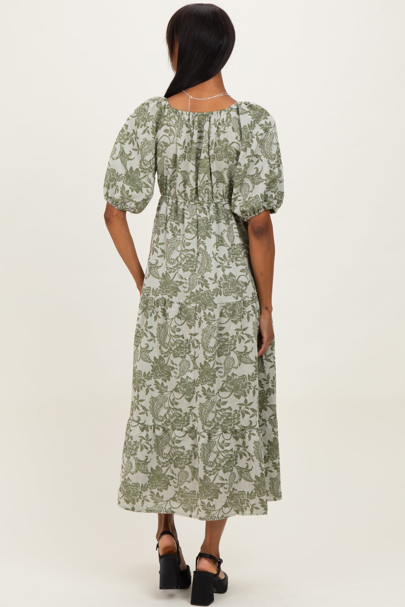 woman wearing a back view of a green floral print midi dress with puff sleeves and a cinched waist