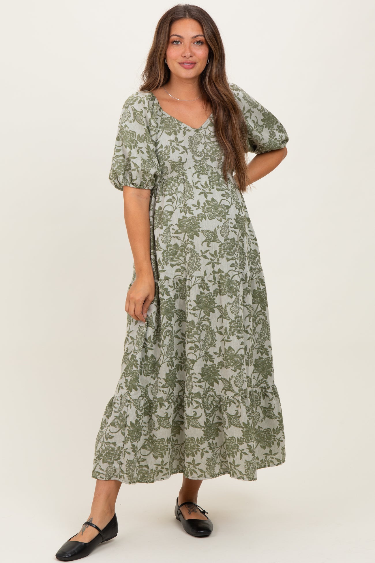 woman wearing a green floral maternity dress with short puff sleeves and a flowy skirt, displaying her baby bump