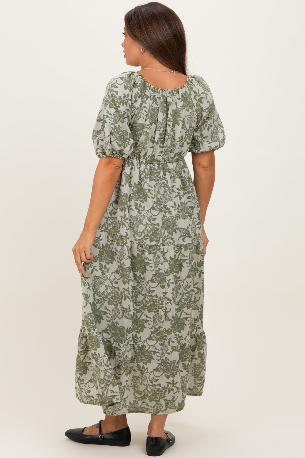 woman wearing a green floral print maternity maxi dress with puff sleeves and a tiered skirt, showing her baby bump