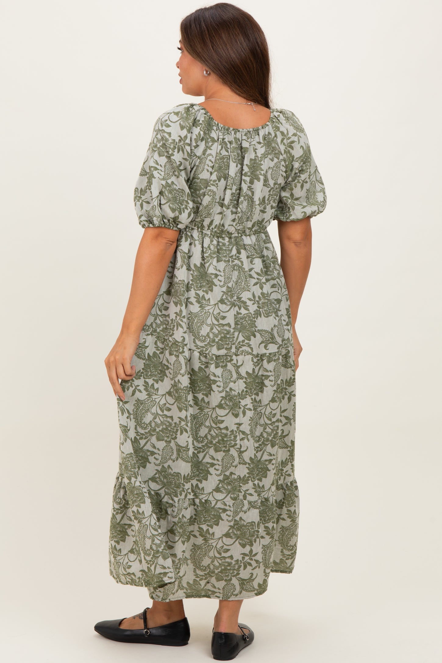 woman wearing a green floral print maternity maxi dress with puff sleeves and a tiered skirt, showing her baby bump