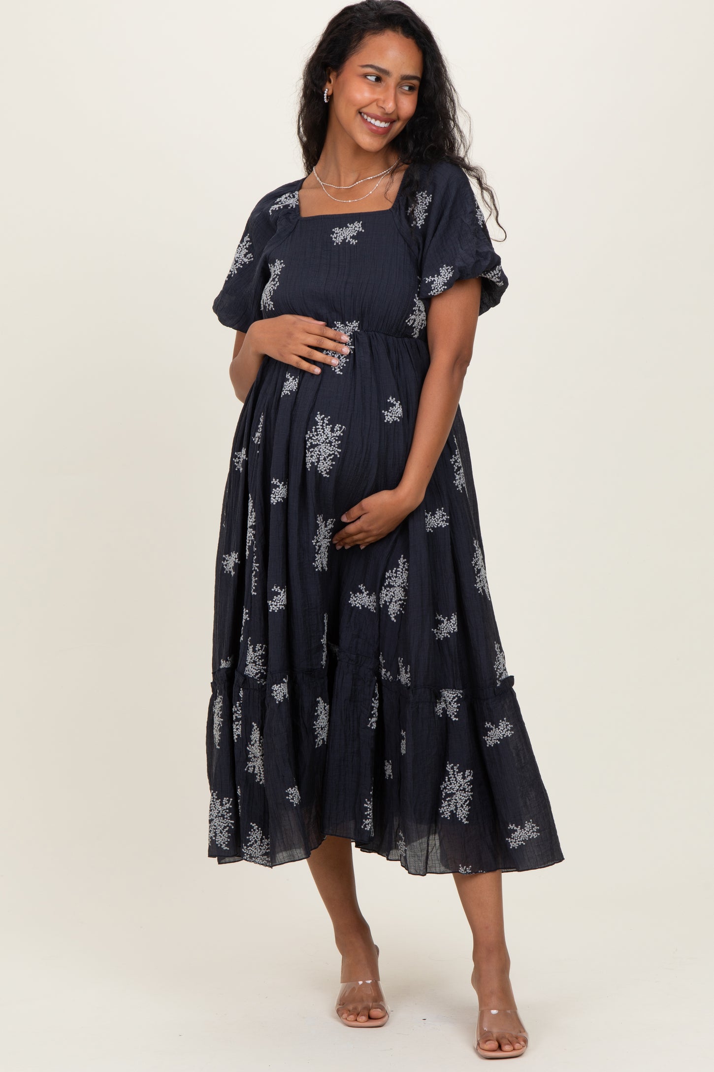 woman wearing a navy blue maternity dress with floral embroidery and short sleeves, holding her baby bump