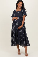 woman wearing a navy blue maternity dress with floral embroidery and short sleeves, holding her baby bump
