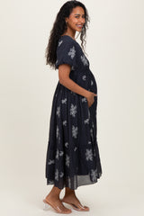 woman wearing a navy blue maternity maxi dress with floral embroidery and holding her baby bump