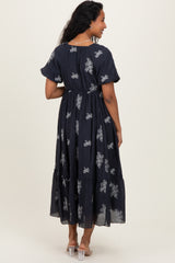 woman wearing a navy blue maternity maxi dress with floral embroidery and tiered design, showing her back
