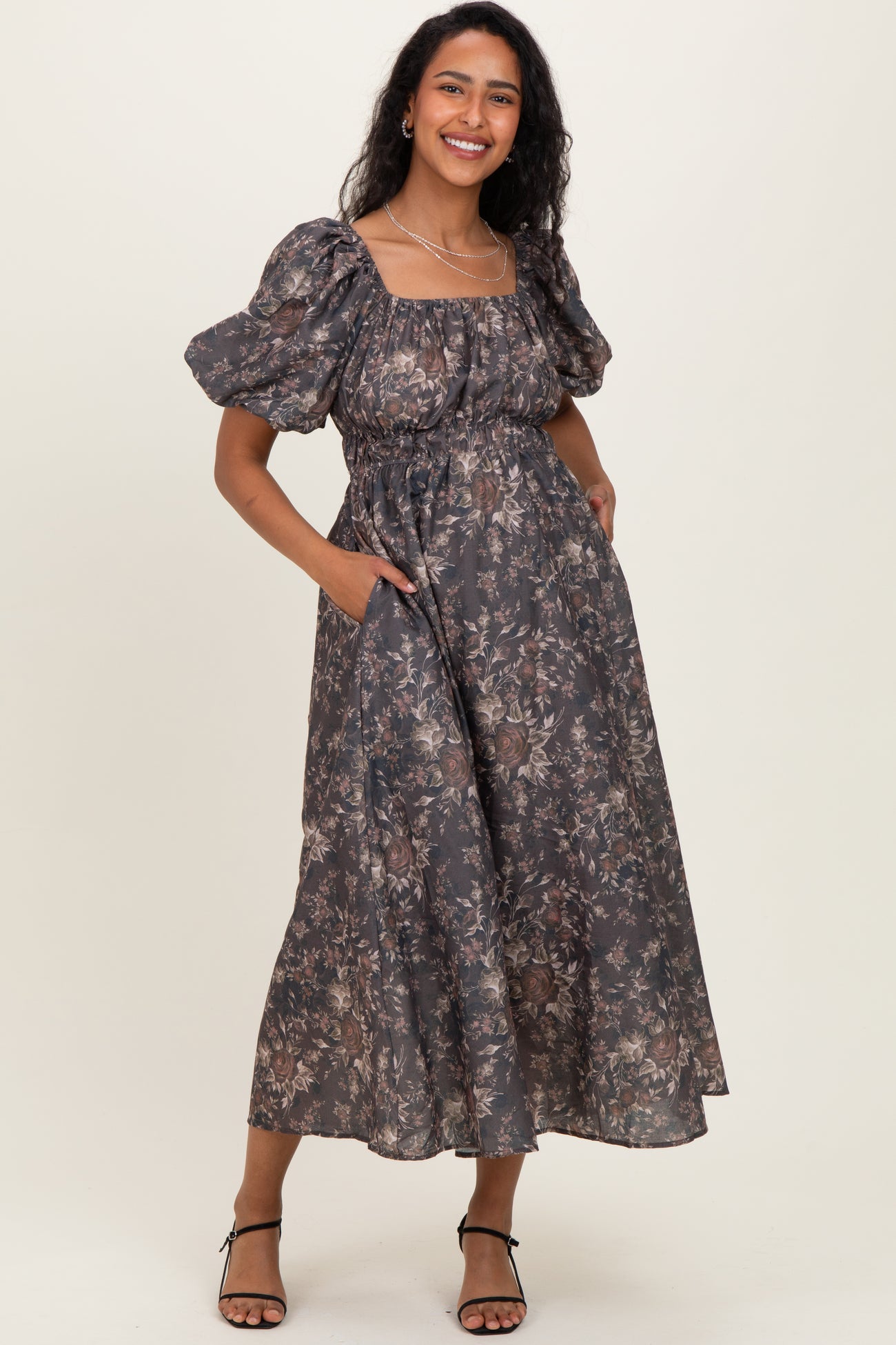 woman wearing a floral print maxi maternity dress with puff sleeves and pockets, showcasing a baby bump