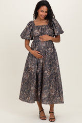 woman wearing a dark floral maternity maxi dress, holding her baby bump while standing gracefully
