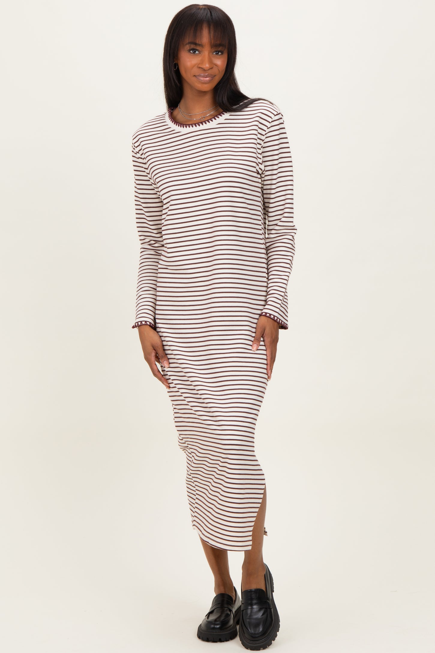 woman wearing a long striped midi dress with long sleeves and side slits, paired with black loafers