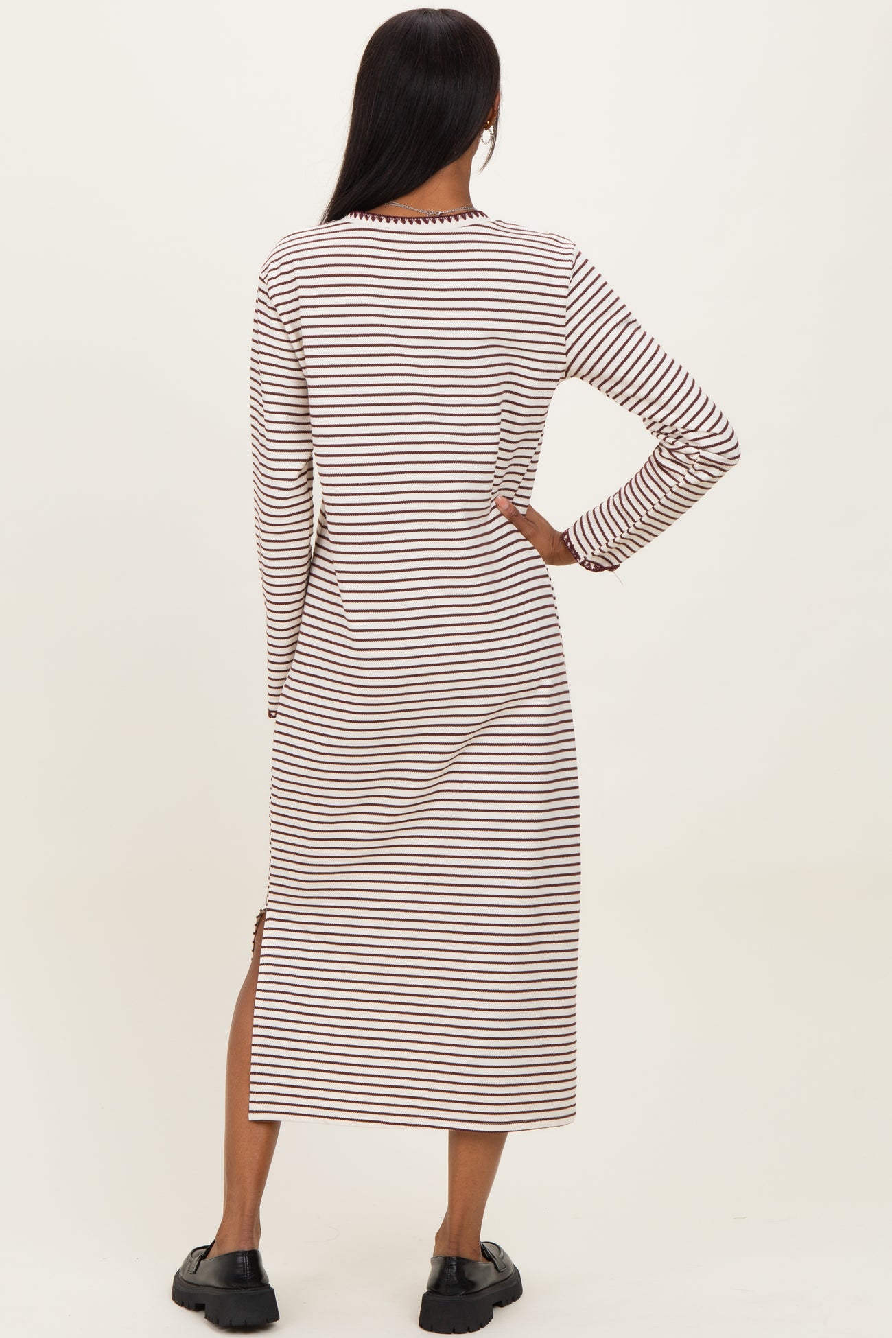 woman wearing a striped long sleeve midi dress with side slits, viewed from the back