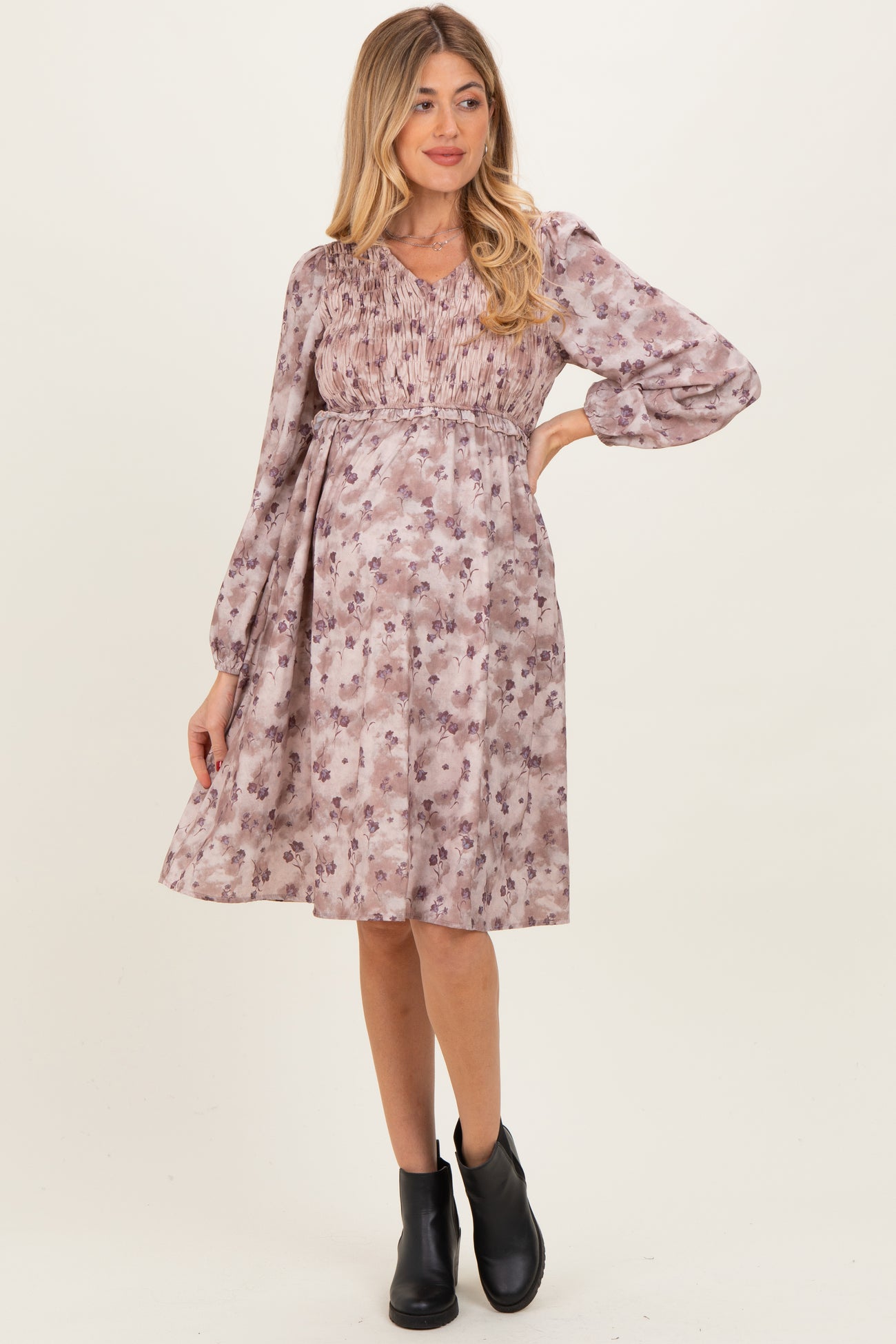 woman wearing a purple floral maternity dress with a smocked bodice and long sleeves, showing her baby bump