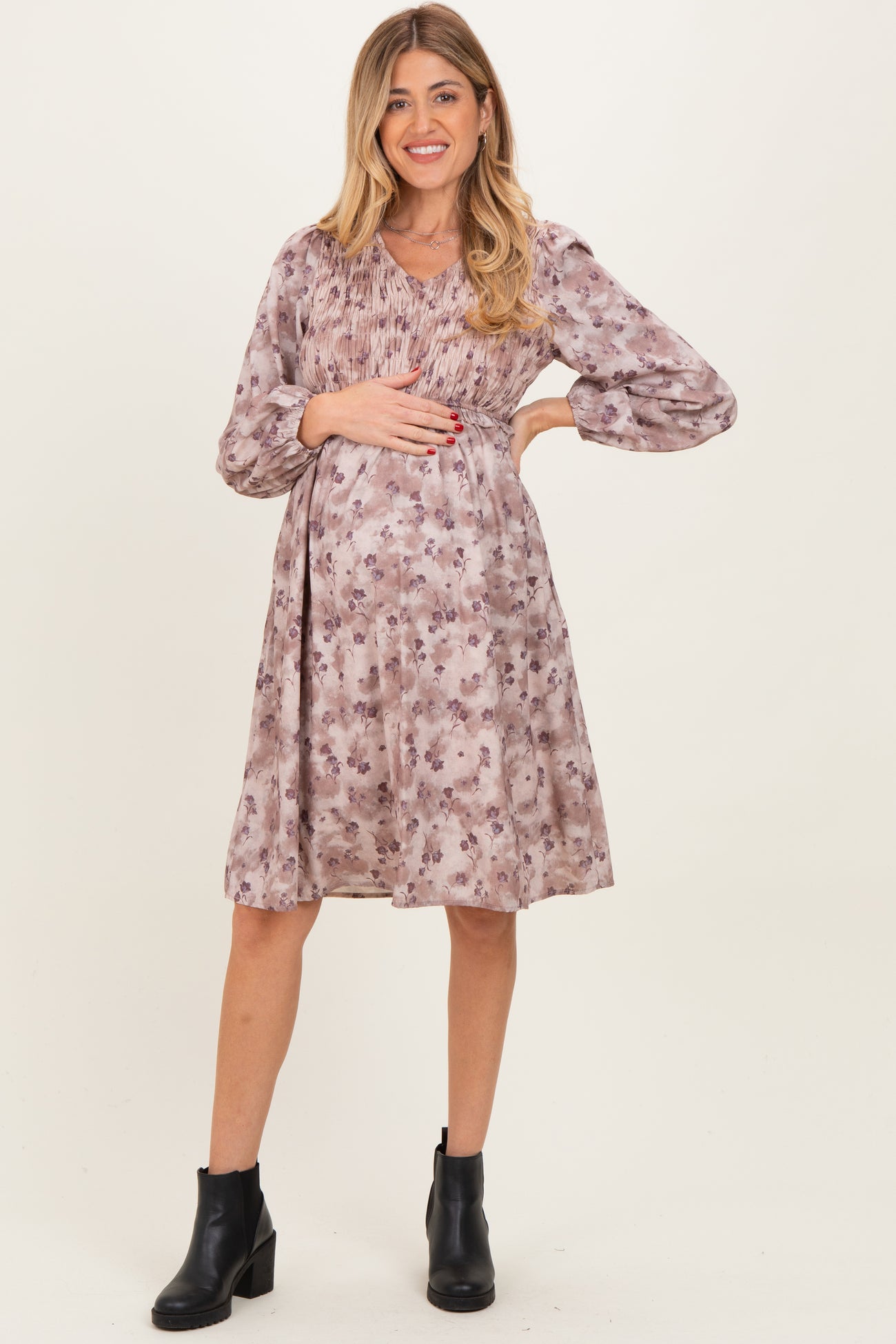 woman wearing a floral print maternity dress with long sleeves and a gathered bodice, holding her baby bump
