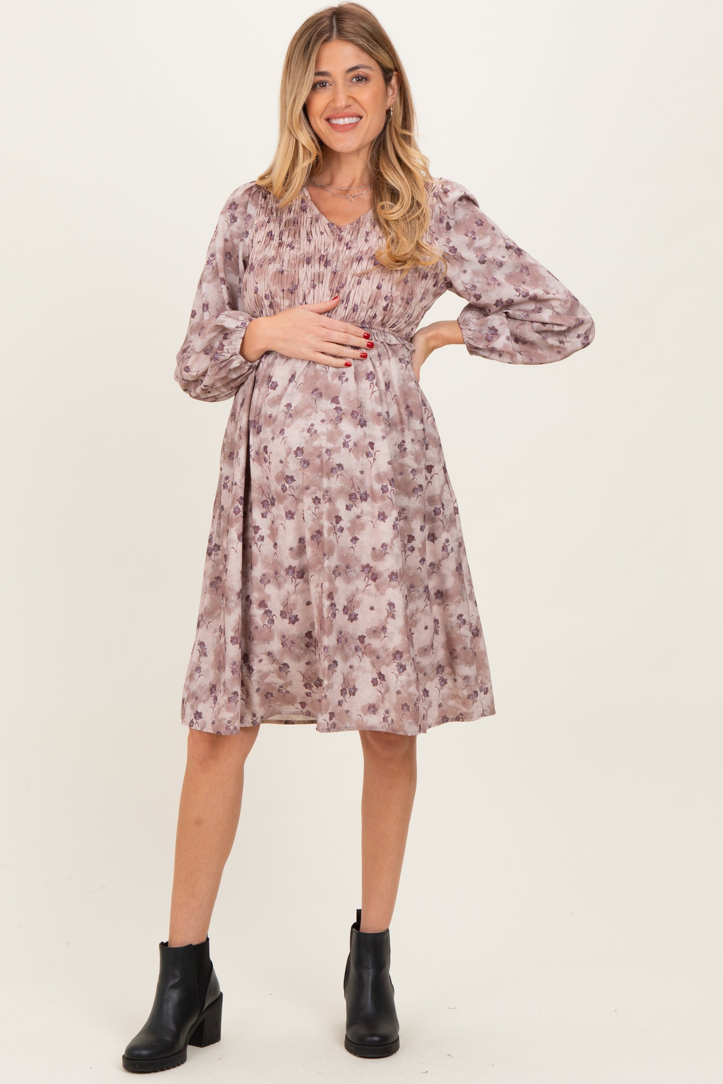 woman wearing a floral print maternity dress with long sleeves and a gathered bodice, holding her baby bump