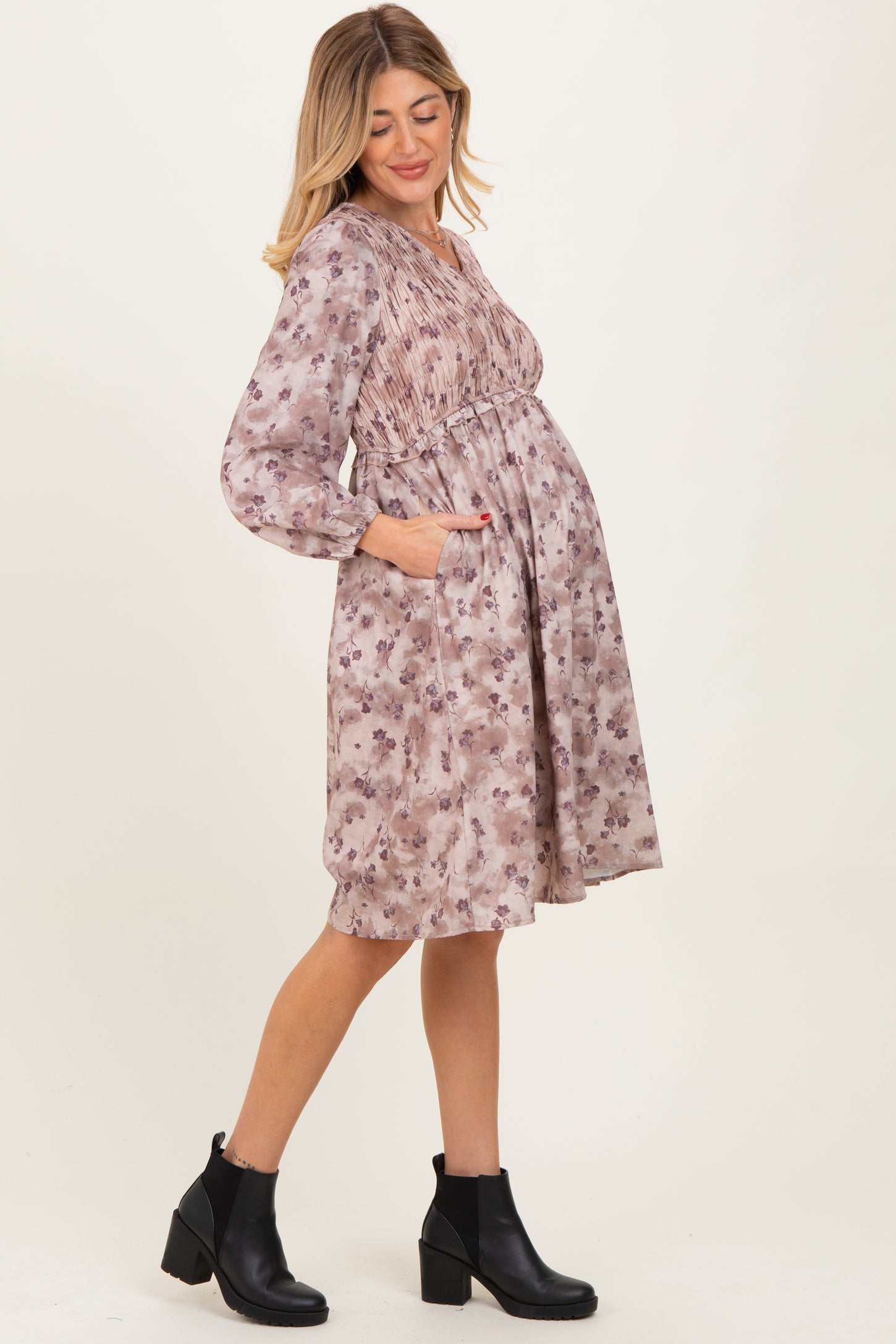 woman wearing a floral maternity dress with smocked bodice and pockets, showing her baby bump, paired with black ankle boots