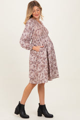 woman wearing a floral maternity dress with smocked bodice and pockets, showing her baby bump, paired with black ankle boots