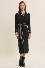 woman wearing a black ribbed long sleeve dress with a collar and contrasting white details, styled with a tie belt
