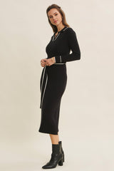 woman wearing a black ribbed knit midi dress with a v-neck and white trim, styled with ankle boots