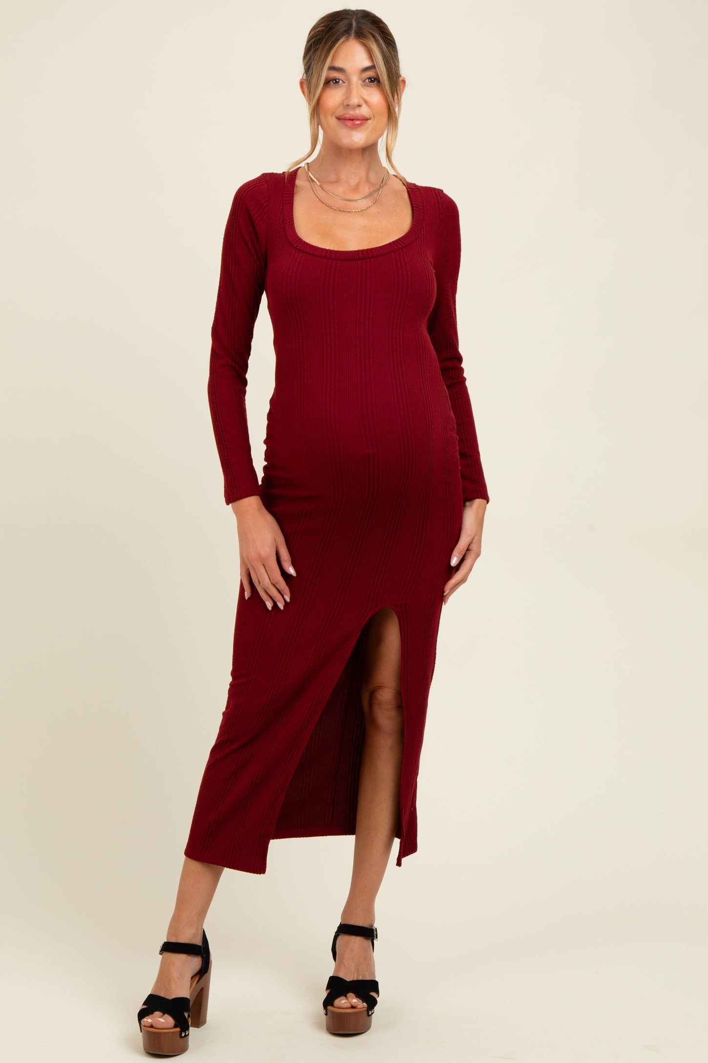 woman wearing a red ribbed maternity dress with long sleeves and a side slit, showcasing her baby bump