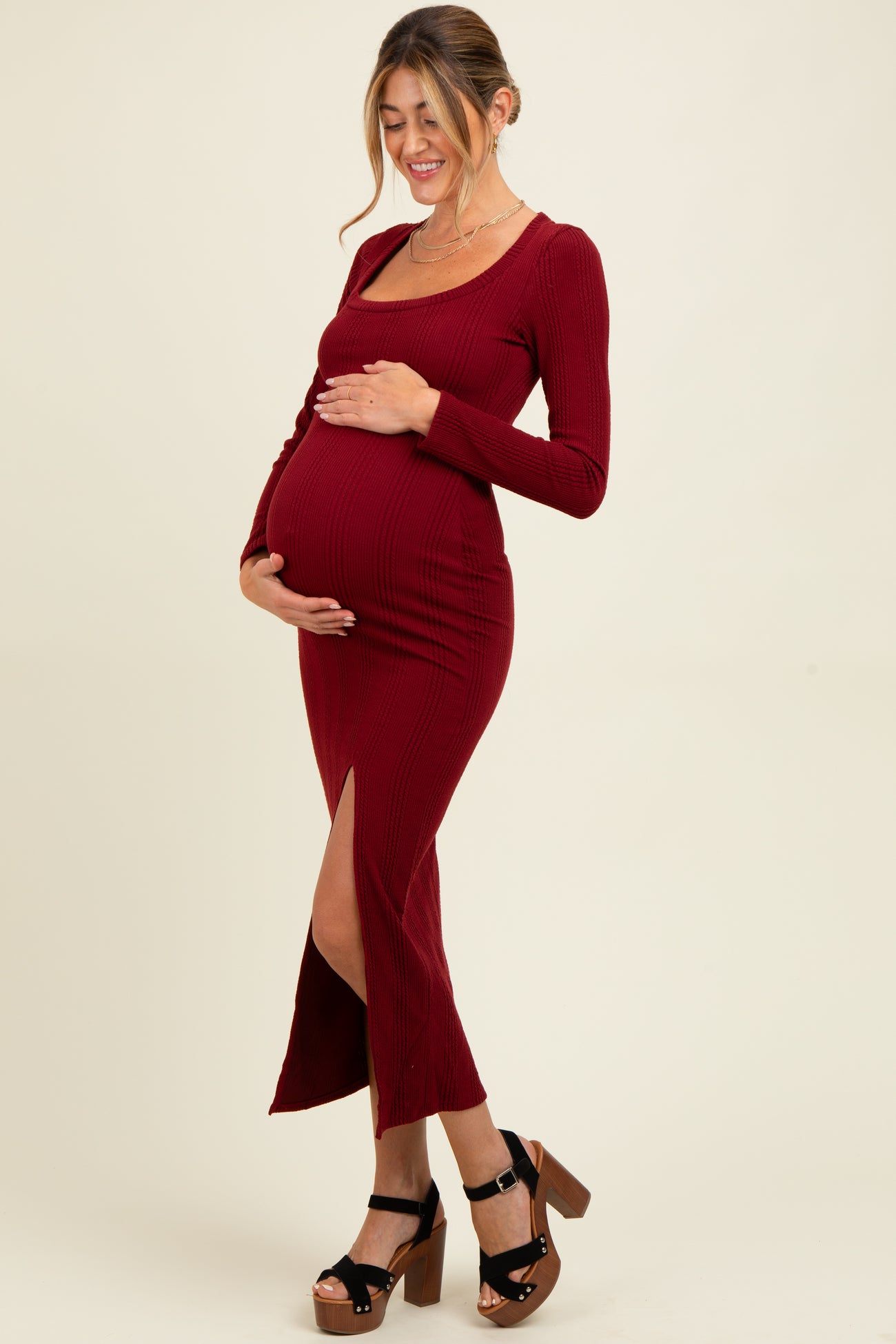 woman wearing a burgundy ribbed maternity dress with a side slit, showcasing her baby bump while smiling