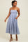 woman wearing a blue and white striped midi dress with floral details and adjustable straps, standing with one hand in a pocket