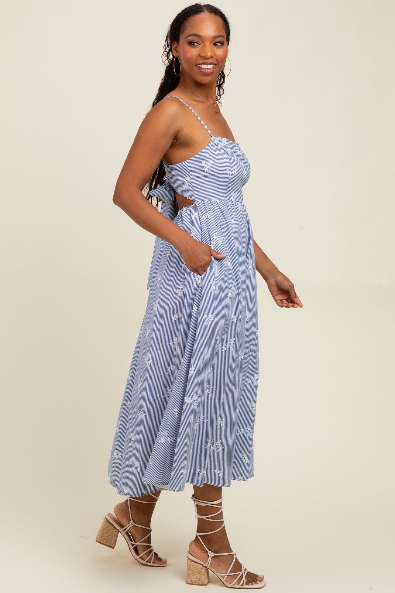 woman wearing a blue and white striped midi dress with floral print and side pockets, standing sideways with a relaxed pose