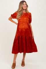 woman wearing an orange maternity dress with short puff sleeves and a tiered skirt, showing her baby bump
