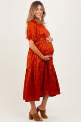 woman wearing an orange textured maternity dress with short sleeves and a tiered skirt, cradling her baby bump