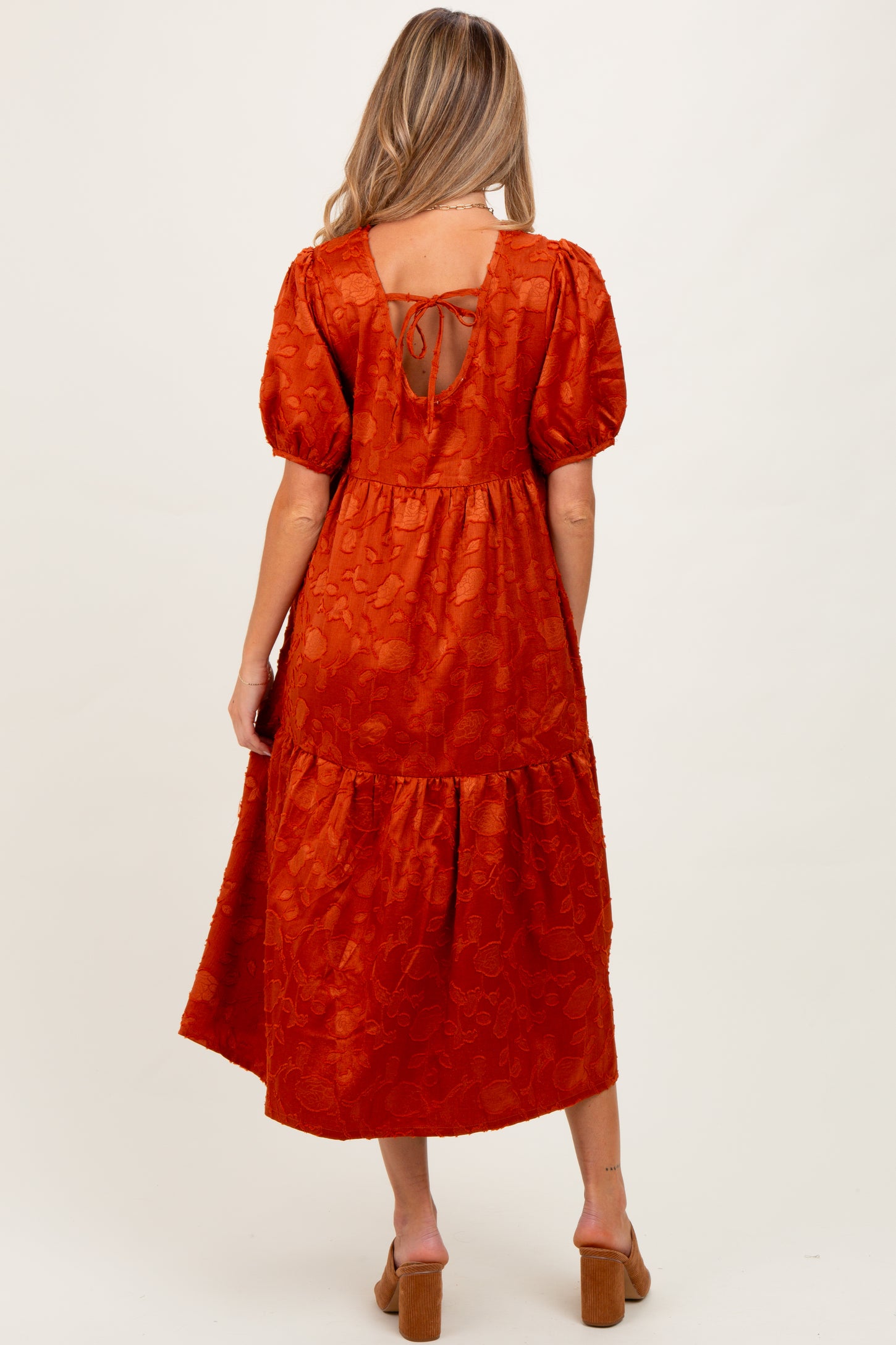 woman wearing an orange maternity dress with puff sleeves and lace-up back, showing a flowing tiered skirt