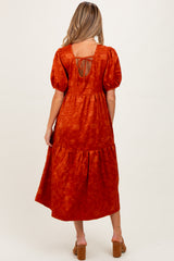 woman wearing an orange maternity dress with puff sleeves and lace-up back, showing a flowing tiered skirt