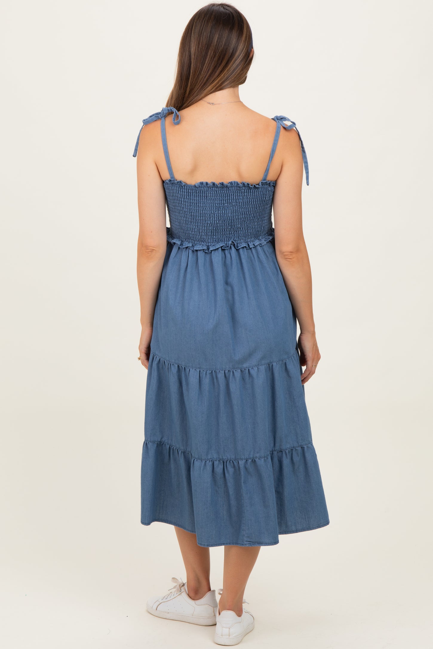 woman wearing a denim maternity dress with tie straps and a tiered skirt, showcasing a comfortable fit for pregnant styles