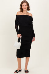 woman wearing a black off-the-shoulder ruched dress with long sheer sleeves and holding a white beaded handbag