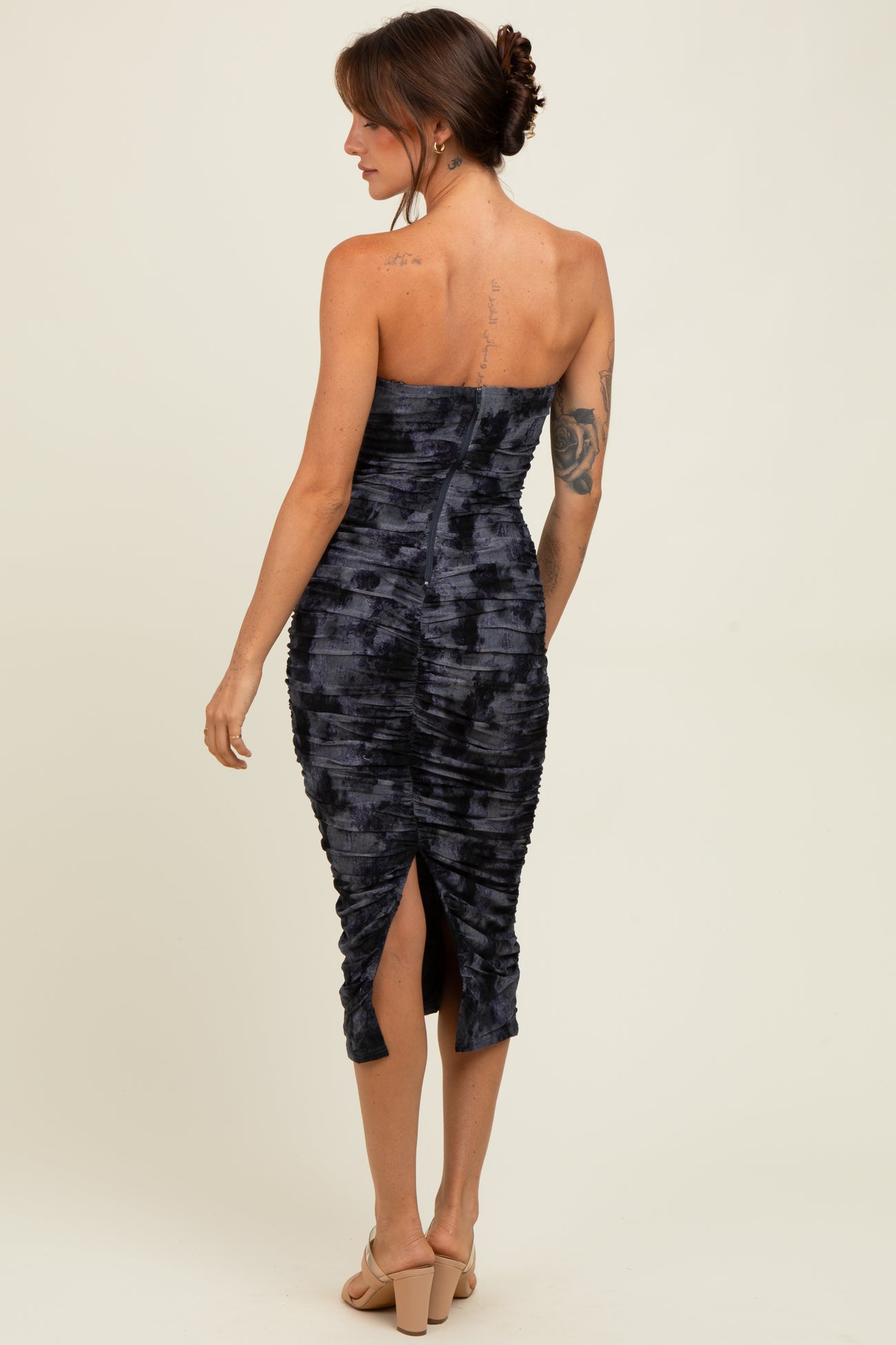 woman wearing a dark blue strapless fitted midi dress with ruching and a back slit, model viewed from the back
