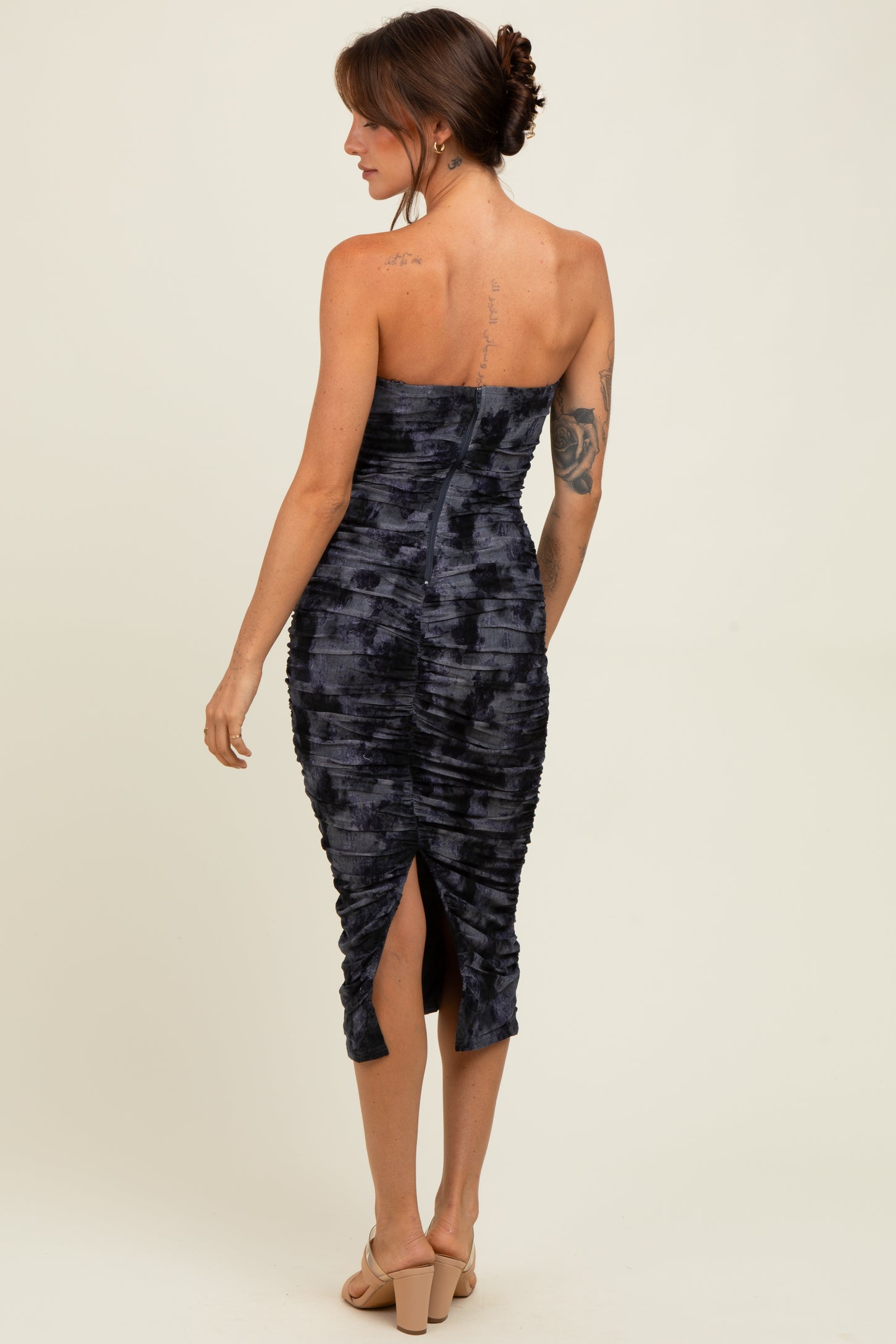 woman wearing a dark blue strapless fitted midi dress with ruching and a back slit, model viewed from the back