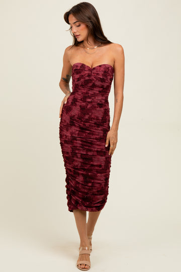 woman wearing a burgundy strapless bodycon dress with ruching details and a straight neckline