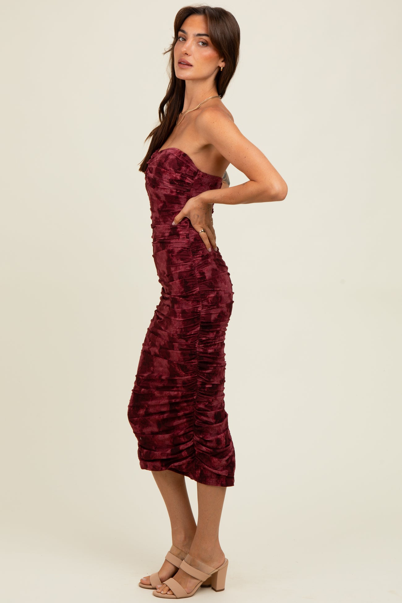 woman wearing a burgundy strapless midi dress with ruched detailing and a fitted silhouette