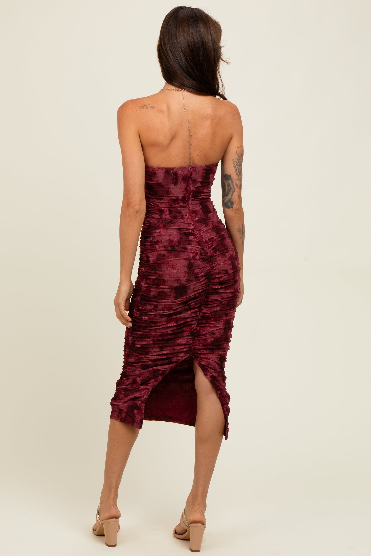 woman wearing a burgundy strapless ruched midi dress with a side slit and back detail