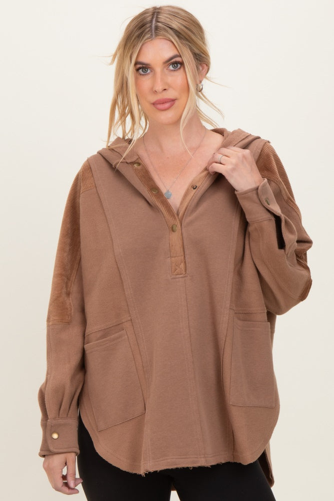 woman wearing a brown oversized hoodie with a button placket and side pockets, styled with black leggings
