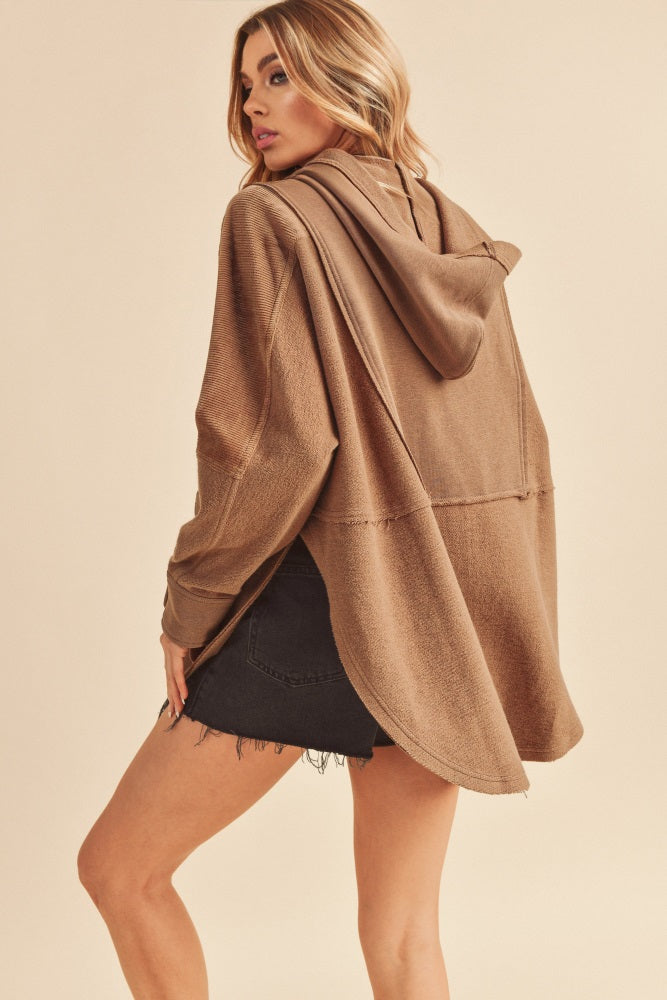 woman wearing a brown oversized hoodie with a hood and a high-low hem paired with a black denim mini skirt