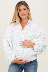 woman wearing a white floral maternity pullover with a collar and puff sleeves, holding her baby bump
