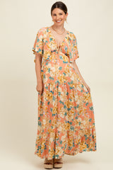 woman wearing a floral maxi maternity dress in pink and yellow, with short flutter sleeves and a tie front detail
