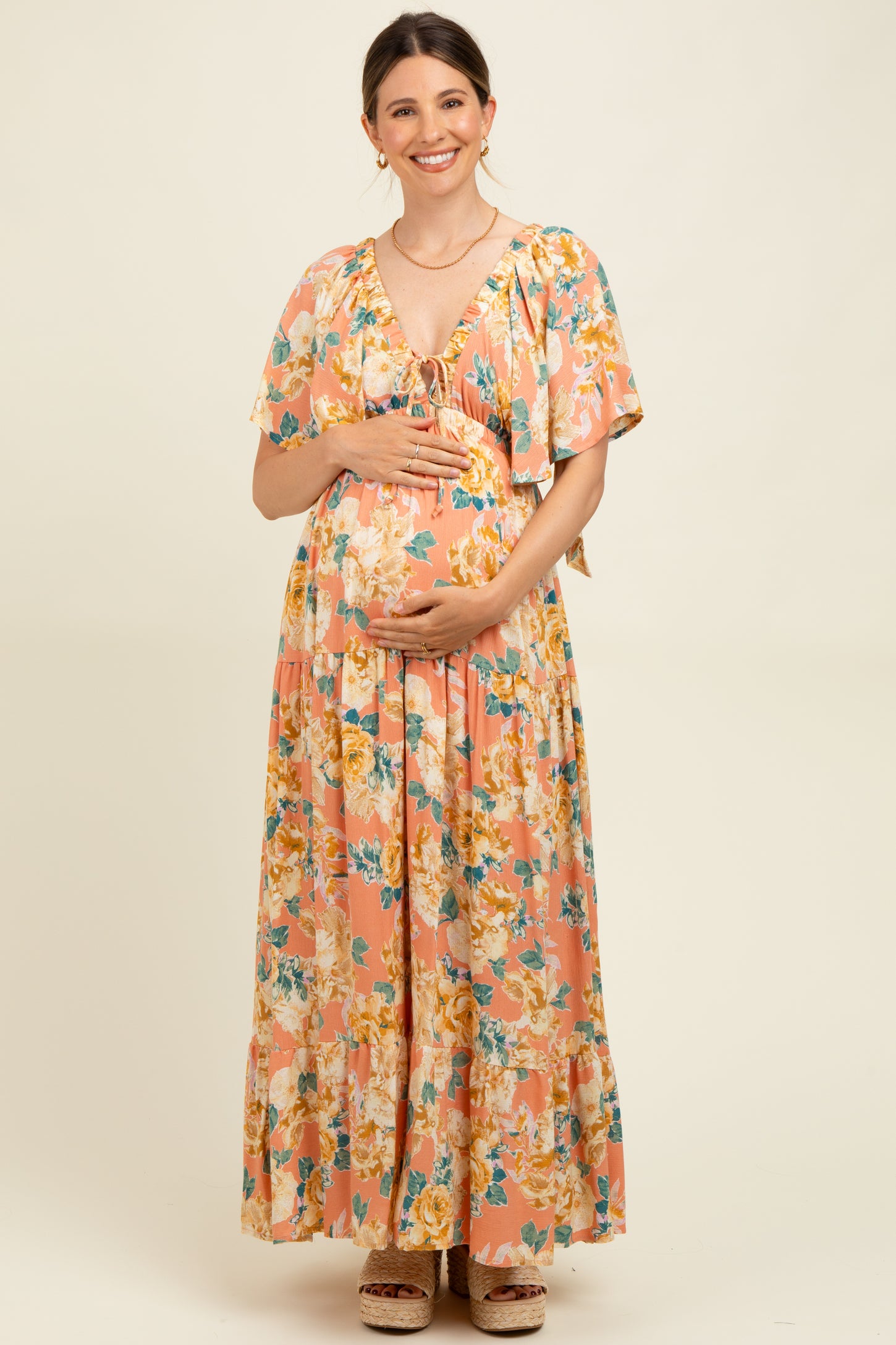 woman wearing a pink floral maternity maxi dress and holding her baby bump