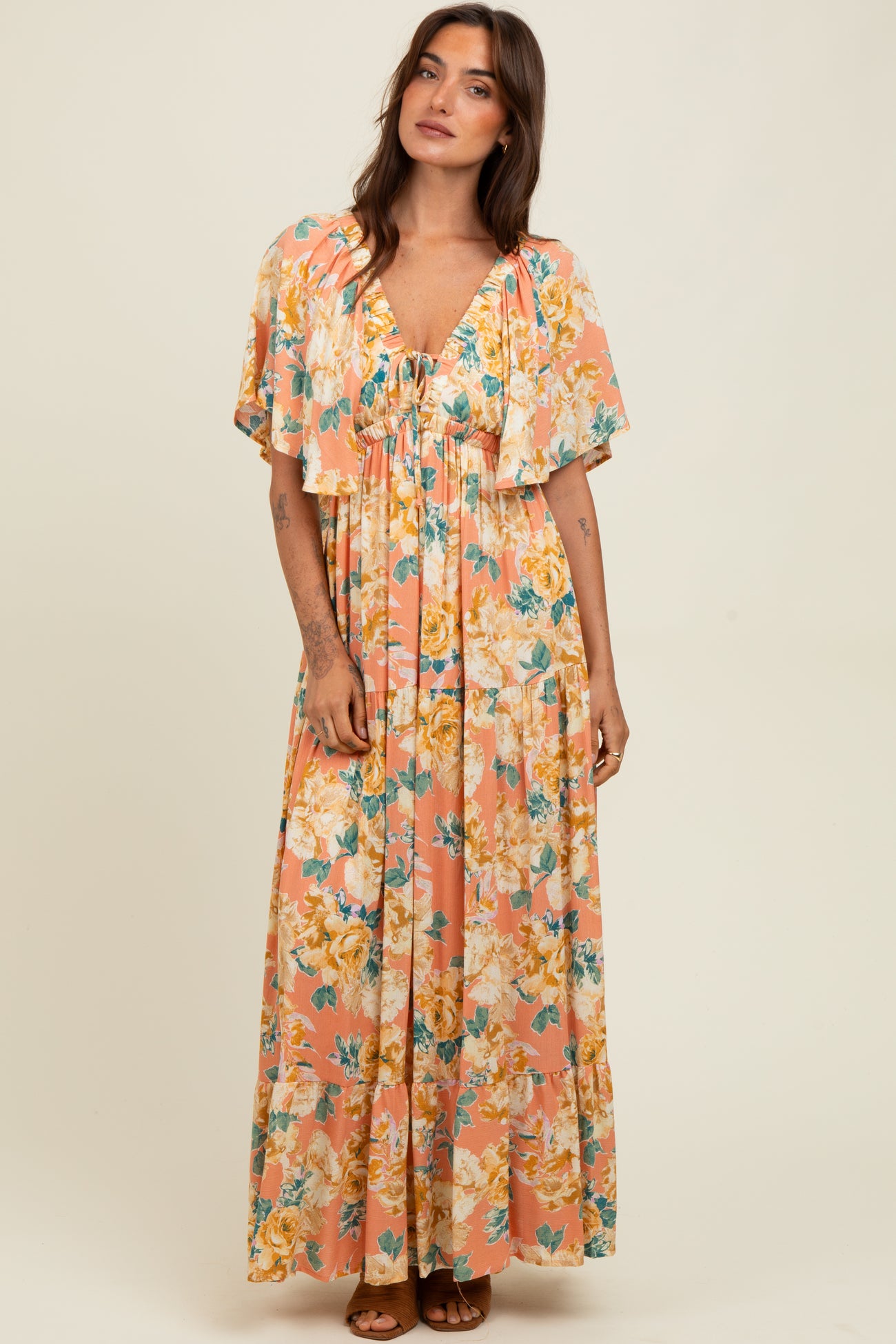 woman wearing a floral maxi dress with flutter sleeves in pink and yellow tones