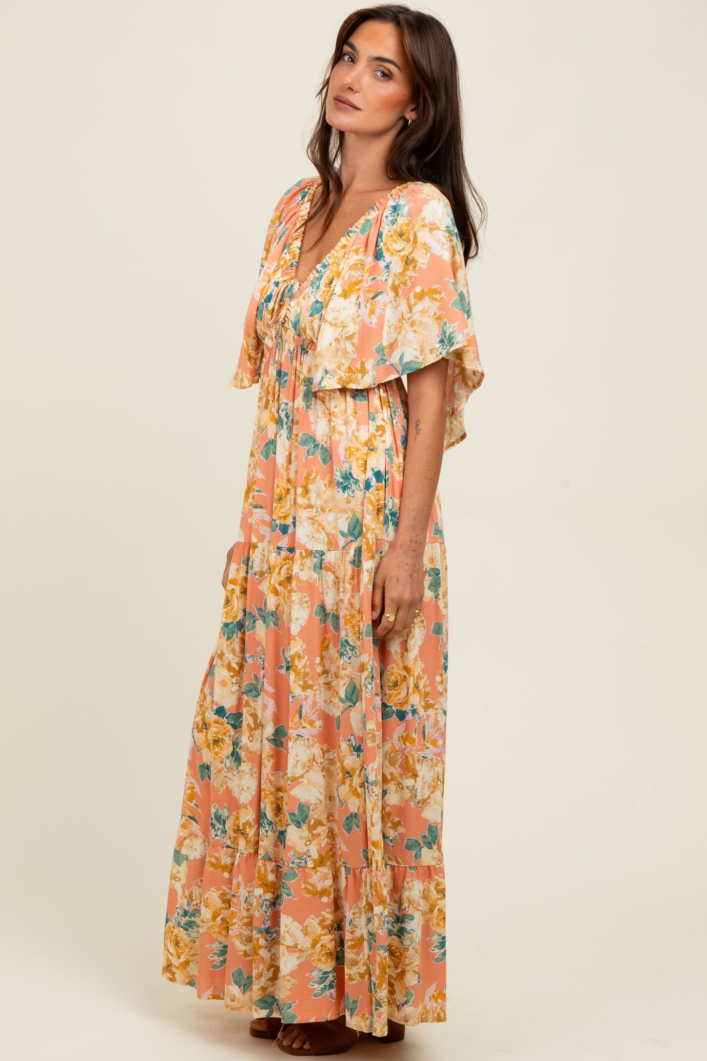 woman wearing a floral maxi dress in peach and yellow tones with flutter sleeves and a tiered skirt