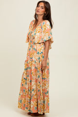 woman wearing a floral maxi dress in peach and yellow tones with flutter sleeves and a tiered skirt