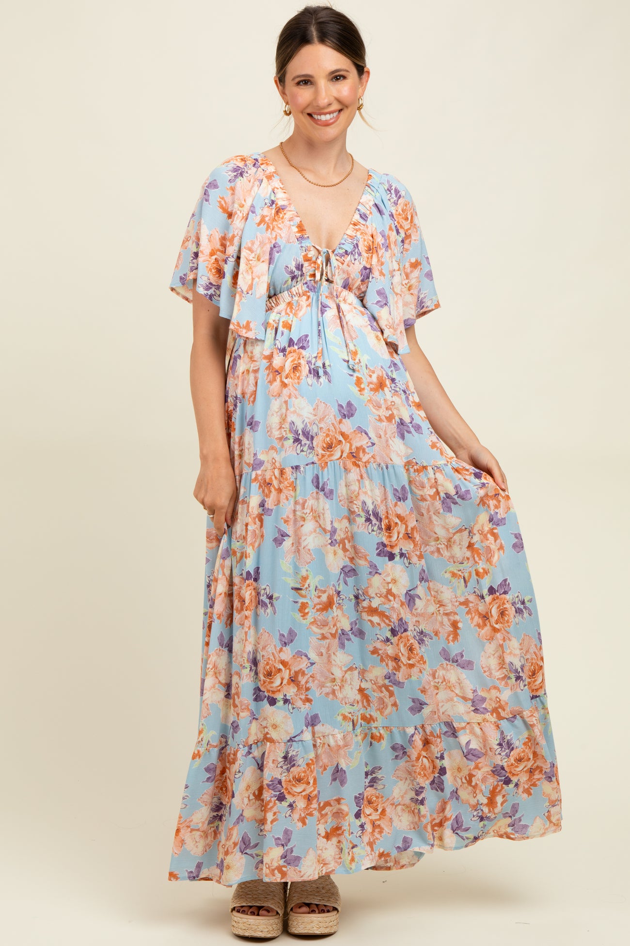 woman wearing a light blue floral maternity maxi dress with a tie-front detail and flutter sleeves, showcasing her baby bump