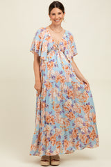 woman wearing a light blue floral maternity maxi dress with a tie-front detail and flutter sleeves, showcasing her baby bump