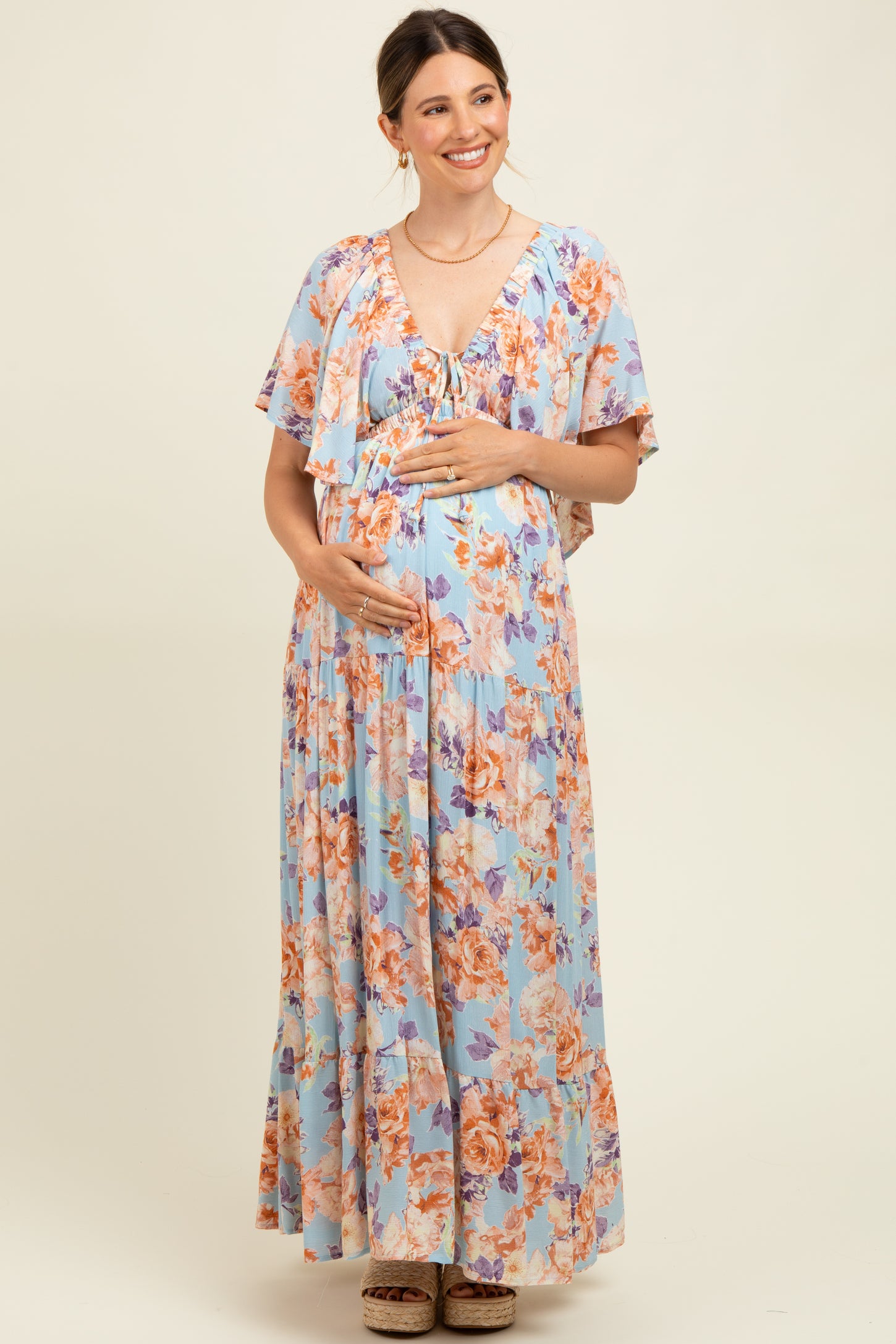 woman wearing a blue floral maternity maxi dress, smiling and holding her baby bump