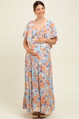 woman wearing a blue floral maternity maxi dress, smiling and holding her baby bump