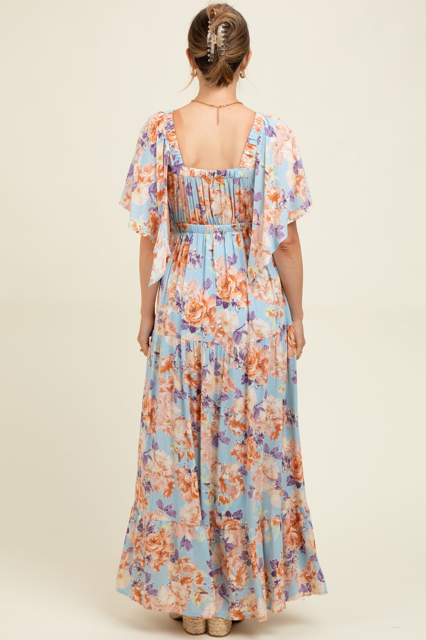woman wearing a light blue floral maternity maxi dress with flutter sleeves, showing the back view