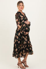 woman wearing a black floral maternity dress with long sleeves and ruffled hem, holding her baby bump